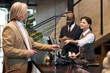 © pressmaster - Group of professionals discussing business transactions at office reception area with modern interior design in background