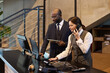 © pressmaster - Professional team engaged in work at a contemporary office, using multiple devices and discussing project details at front desk. Dynamic setting with a blend of technology and human interaction