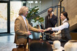 © pressmaster - Businessman making payment at hotel reception desk while receiving assistance from reception staff, with lobby environment in background