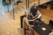 © pressmaster - Group discussing work assignment near desk in modern office setting with a staircase in background. Various office equipment including computers and phones are visible
