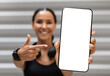 © Prostock-studio - Fitness App. Sporty Young Woman Pointing At Big Blank Smartphone In Hand, Fit Millennial Lady Showing Phone With White Screen, Demonstrating Copy Space, Recommending New Mobile Application, Mockup