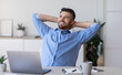 © Prostock-studio - Smiling millennial businessman leaning back in chair at workplace, resting after successful day in office