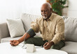 © Prostock-studio - Mature African American Man Measuring Arterial Blood Pressure With Sphygmomanometer Medical Device Sitting On Couch Indoors. High Blood-Pressure, Hypertension Health Problem Concept