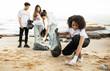 © Prostock-studio - Happy young multiethnic people volunteers in t-shirts with garbage packages clean up garbage, plastic bottles on sea beach, outdoor. Environment conservation, protecting eco