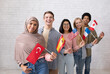 © Prostock-studio - Modern exchange program and language learning. Happy young international students looking at camera and holding flags of their countries, on white brick wall background, studio shot, copy space