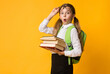 © Prostock-studio - Back To School. Surprised Primary School Girl Carrying Stack Of Heavy Books Over Yellow Background. Copy Space