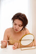 © looking2thesky - Stressed sad brunette young woman wearing beige top looking at mirror and touching her face having skin problems. Acne, pimples, wrinkles, dull skin