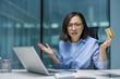 © Liubomir - A frustrated asian woman at her desk, holding a credit card and looking confused. She faces a laptop in her office setting.