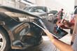 © chartphoto - Technician evaluates vehicle damage using a digital tablet at an auto repair shop, likely for insurance or repair documentation.