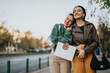 © qunica.com - Two women, one leaning on the other's shoulder, share a bright smile while standing together in an outdoor city environment.