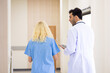 © NVB Stocker - Back view : Multi-ethnic healthcare workers in hospital. nurse and doctor walking in corridor and  talking and in discussion for advice, medical service, diagnosis and consulting