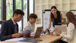 © matinee - Confident female team leader presenting ideas to colleagues in a collaborative office.