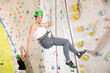 © JackF - Sporty cheerful young female climber in helmet using safe rope going down after training in bouldering amusement center