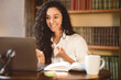 © Prostock-studio - Online Video Call And Communication. Portrait of smiling curly woman sitting at table, using laptop and having virtual conference on computer, talking to webcam, explaining plan, selective focus