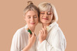 © Pixel-Shot - Happy young woman and her mother in bathrobes with bottles of cosmetic oil on beige background
