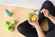 © Pixel-Shot - Sporty young woman sitting on yoga mat with bowl of nutritious oatmeal and dumbbells at home, top view