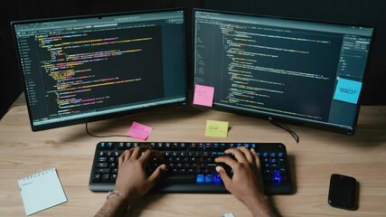 A programmer coding on dual monitors with colorful sticky notes in a modern workspace
