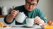 © NN AI - Young man with down syndrome wearing glasses pouring tea from teapot into cup at home. Person with special needs enjoying hot beverage in kitchen. Inclusion, independent living. Home care service sale