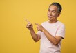 © Anwar Fauzan - A grandfather in a soft pink T-shirt points at it with a surprised and curious expression, as if seeing something unexpected. The plain bright yellow background emphasizes his animated