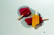 © VISTA by Westend61 - Three melting popsicles in red and yellow on a surface under sunlight