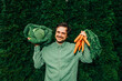 © VISTA by Westend61 - Man in green shirt holding carrots and Italian kale outdoors