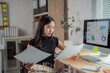 © Tj - Focused Asian businesswoman comparing statistics document with data displayed on computer screen, working with financial graphs charts, analyzing marketing research results in office