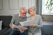 © Юлия Завалишина - Sad tired disappointed middle aged senior couple sit with paper document. Unhappy older mature man woman reading paper bill managing bank finances calculating taxes planning loan debt pension payment