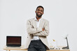 © SHOTPRIME STUDIO - Confident young African American man with short hair and beard, wearing casual beige blazer and white shirt, standing with crossed arms in modern office setting, smiling. People lifestyle concept.