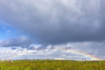 Wall Mural - grey rainy clouds and rainbow over green city park