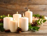 Five lit white candles arranged with evergreen boughs and pinecones on a rustic wooden surface