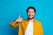 © deagreez - Smiling man in yellow shirt showing thumbs up against blue background symbolizing positivity and confidence