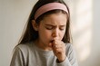 © Iurii - Young girl quietly coughing while sitting indoors in natural light