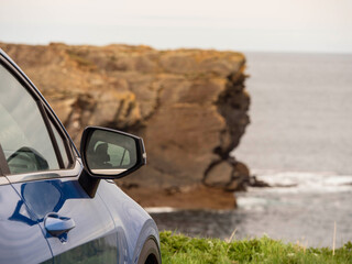 Wall Mural - A blue car is parked on the side of a road next to a cliff overlooking the ocean. Travel and tourism. Trip to nature, cloudy day, rough stone coast. Sightseeing landmarks. West of Ireland.
