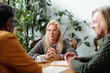 © pressmaster - Senior blonde woman engaging in discussion with two colleagues over coffee in a bright office with plants in background creating a warm, collaborative atmosphere