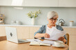 © Юлия Завалишина - Middle aged senior woman sit with laptop and paper document, Pensive older mature lady reading paper bill pay online at home managing bank finances calculating taxes planning loan debt pension payment