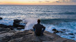 © Yevhenii - Man sitting on rocky shore at sunset contemplating the ocean waves in peaceful solitude