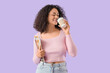 © Pixel-Shot - Young African-American woman with fashion magazine drinking coffee on lilac background