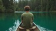 © piyawat - Serene young man in green tshirt sitting in canoe, admiring lake view surrounded by pine trees under cloudy sky.
