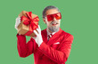 © Studio Romantic - Merry Christmas and Happy New Year concept. Thoughtful grey haired Santa Claus wearing bright red costume, sunglasses and white gloves, holding gift box, isolated over vivid green background