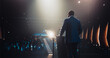 © Gorodenkoff - Confident Thought Leader Walking to a Tribune with laptop Computer, Delivering an Inspiring Presentation About Innovation at Technology Conference. Black Man Talking to an Audience in a Dark Venue