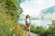 © Andrei - Glowing with joy, a woman strolls a nature trail wrapped in greenery, grinning as mountains and a sparkling lake unfold her perfect summer reset