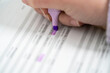 © Studio Marmellata - A person's hand uses a purple highlighter pen to mark specific numbers on a printed document. This process involves reviewing and emphasizing key figures within a financial report or data sheet.