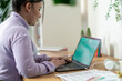 © Studio Marmellata - A young woman sits at a wooden desk, typing on her laptop. She is working or studying from home in a bright room with plants and papers.