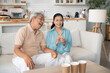 © winnievinzence - Asian senior couple playing toss ping pong ball to the cup in the living room at home on weekend after retirement. Healthy insurance concept