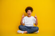 © deagreez - Excited young boy pointing upward while sitting cross-legged against a bright yellow background in casual attire