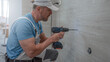 © Sabrewolf - Installation of bathroom furniture. Drilling into the wall through a pre-drilled tile. The plumber works with cordless drill.