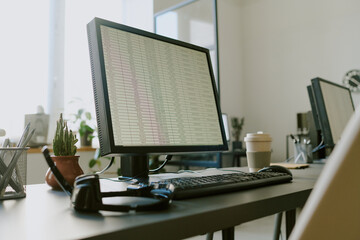 Wall Mural - Office workspace featuring monitor displaying spreadsheet with coffee cup, keyboard, and headphones adding productivity tools to clean, modern desk setup