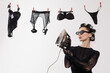 © st.kolesnikov - Stylish woman in black lace outfit with hair curlers and sunglasses playfully holding iron, with black lingerie drying on line in humorous retro domestic scene.