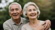 © velikiyzayats - Happy elderly Asian couple smiling and embracing outdoors. Senior man and woman enjoying retirement together, looking joyful and content in a park setting.