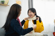 © WMSTUDIO - Two Young Women Enjoying a Cozy Indoor Moment While Tying Scarves and Laughing in a Bright, Warm Living Room Setting